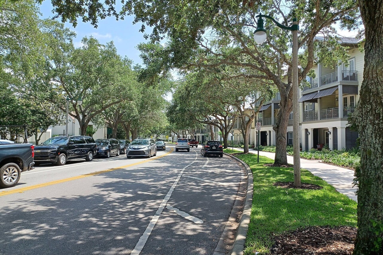Rua arborizada com sobrados de varanda e carros estacionados