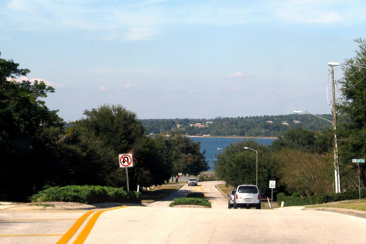 Rua arborizada em declive com o Lago Minneola ao fundo.