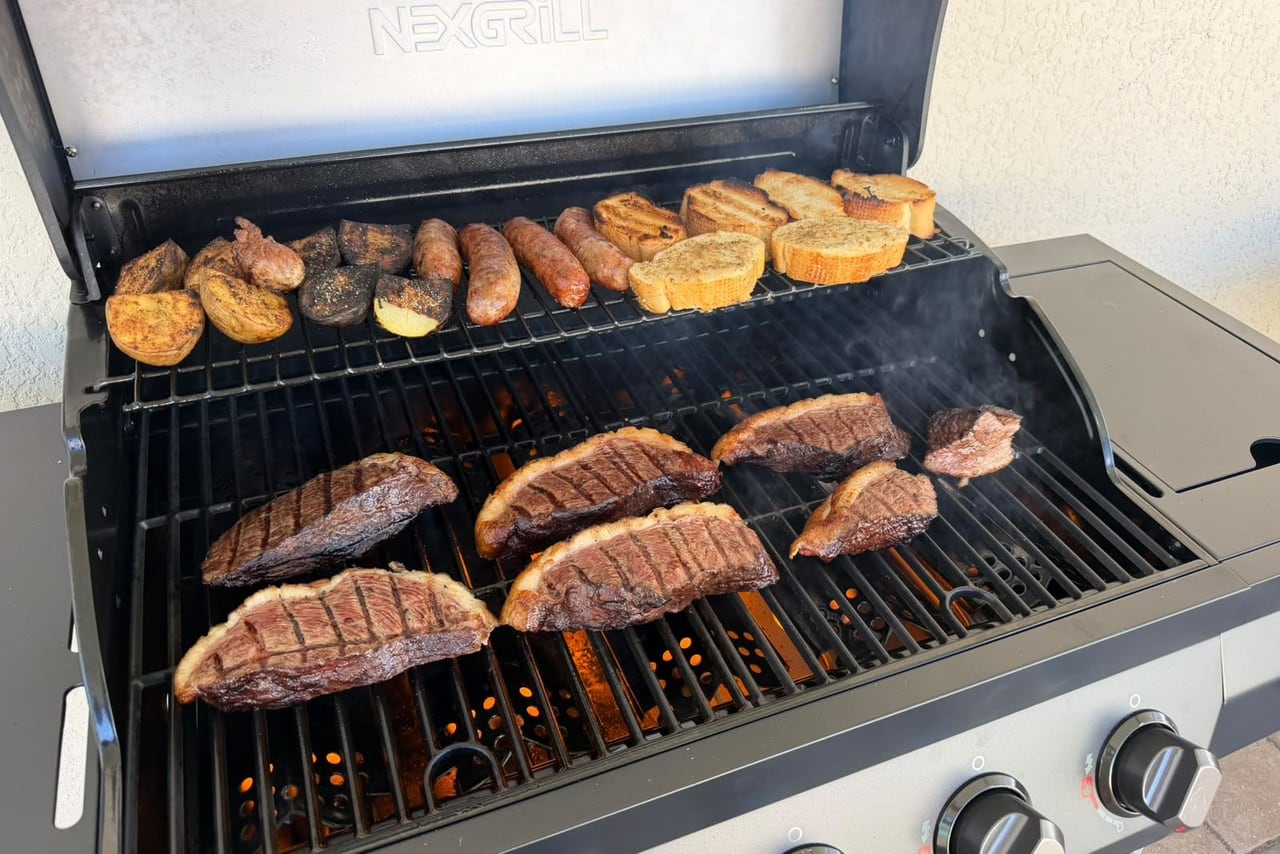 Churrasqueira a gás com picanha, linguiça e pão de alho assando no quintal